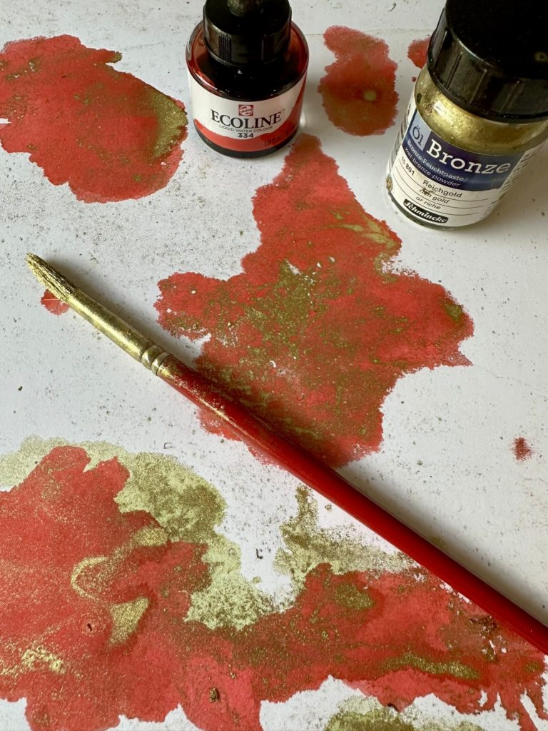 Abstraktes rot-goldenes Gemälde mit Pinsel und kleinen Farbfläschchen auf einem Arbeitstisch.