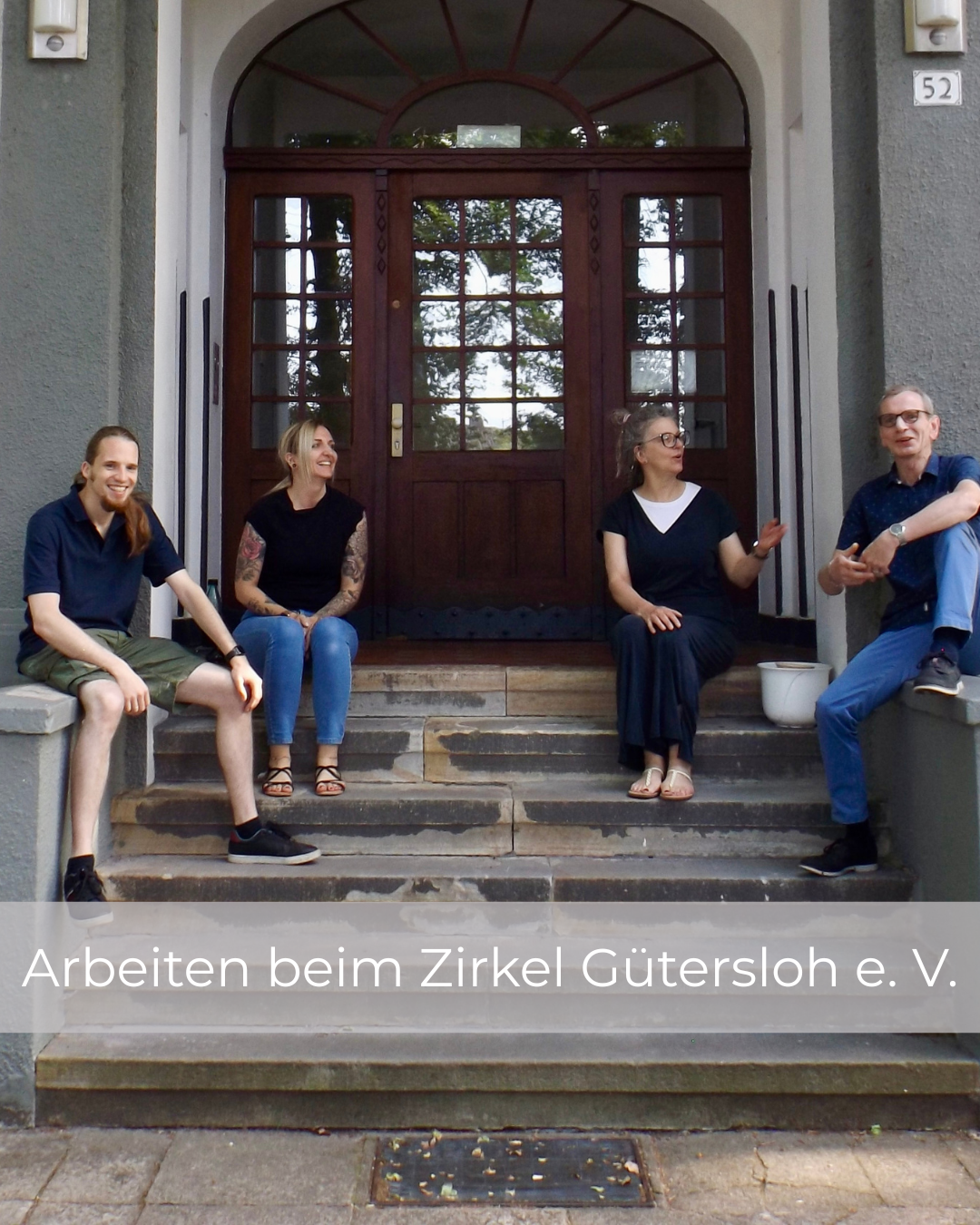 Team der ambulanten Wohnbetreuung des Zirkels Gütersloh sitzt gemeinsam vor dem Eingangsbereich eines Gebäudes.