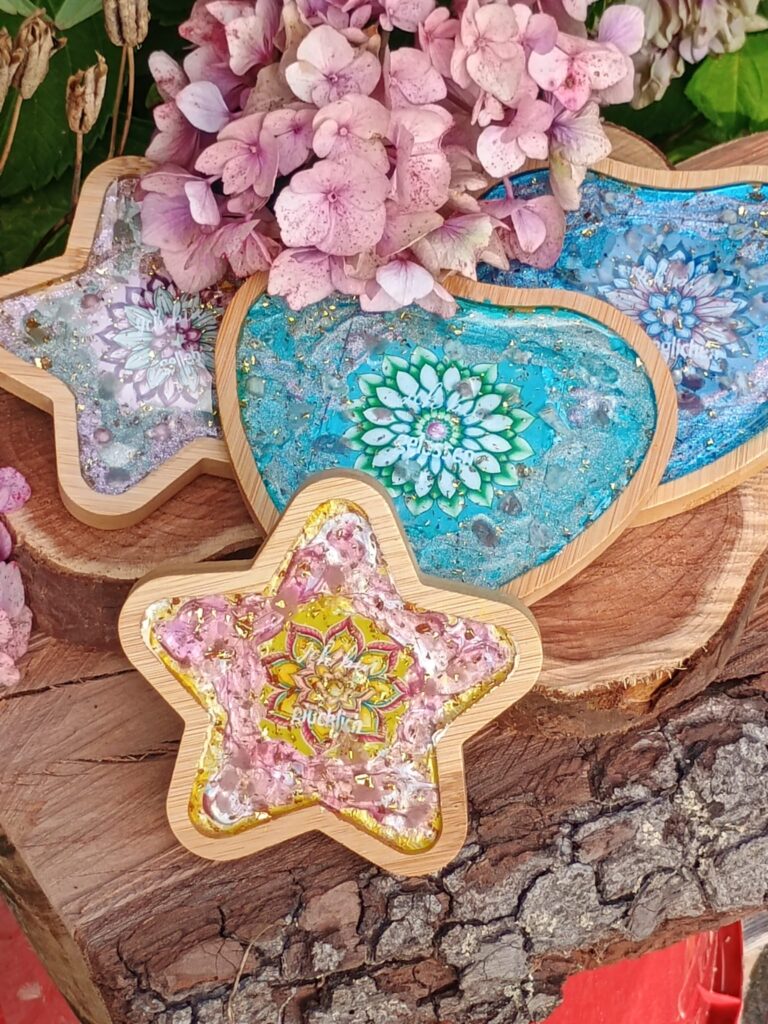 Mehrere „ICH BIN“-Untersetzer aus Orgonit mit eingearbeiteten Symbolen, Farben und Edelsteinen auf einem Tisch arrangiert.