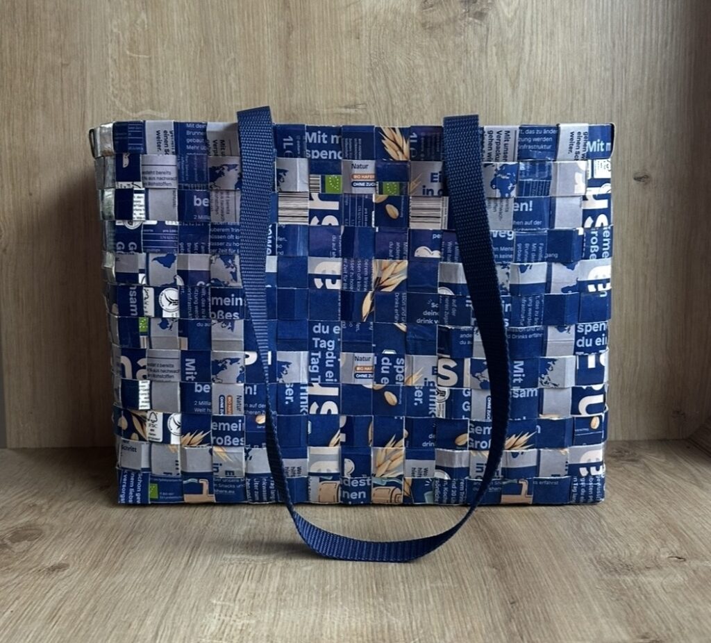 Handgeflochtene Tasche von Kerstin Ruschke aus recycelten Tetrapacks in Blau- und Weißtönen mit langen Tragegriffen.