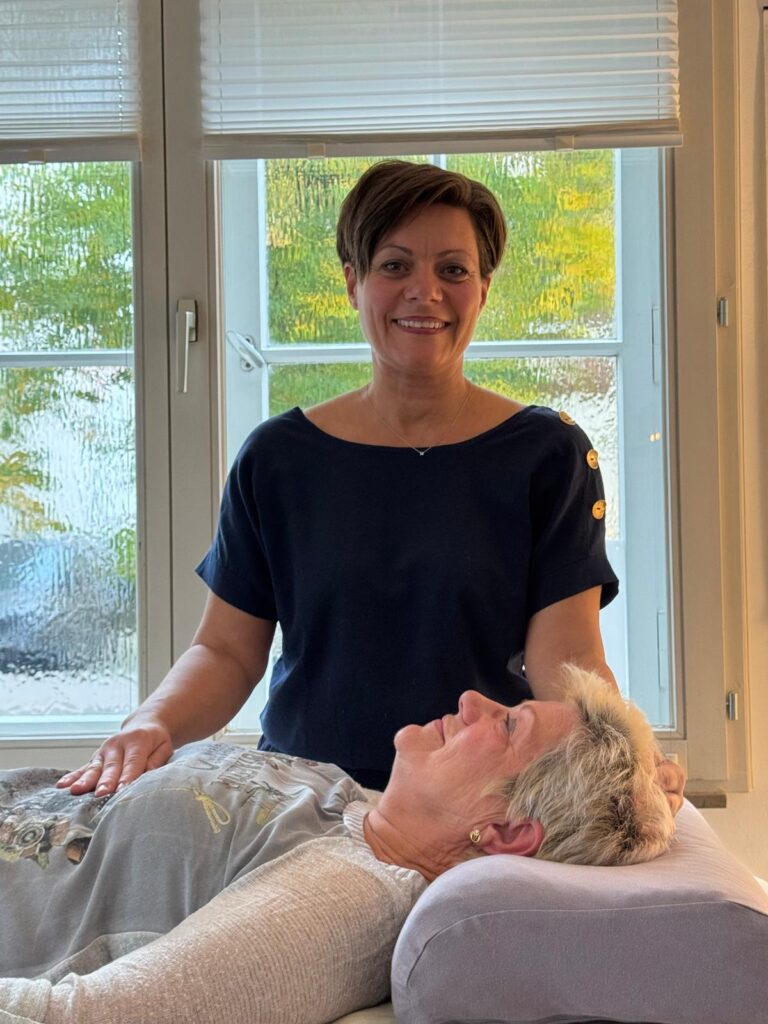 Nicole Willing zeigt gemeinsam mit einer Klientin die Anwendung ihres SomnoBalance®-Nackenstützkissens, das Entspannung und nächtliche Regeneration unterstützen soll.